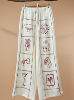 Carregar imagem no visualizador da galeria, Calças brancas de gaze com bordados - vista frontal com patches temáticos
