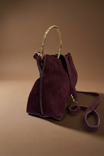Cargue la imagen en el visor de la galería,Clutch bordeaux em vista lateral com aro dourado, fundo castanho quente
